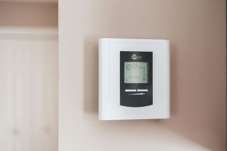 A white digital thermostat mounted on a beige wall next to a closed white door.