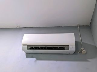 A white wall-mounted air conditioner unit with a power cord connected to a small wall outlet.